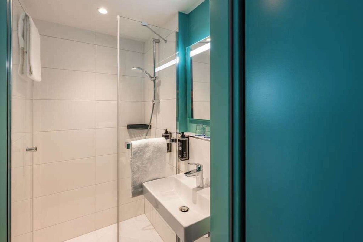 Un baño moderno con cabina de ducha de vidrio, un lavamanos blanco y una pared de acento color aguamarina.
