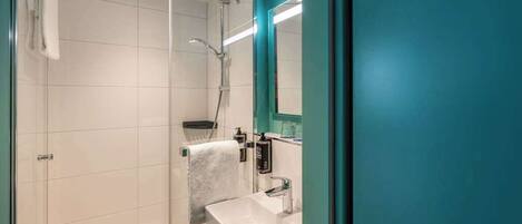 Un baño moderno con cabina de ducha de vidrio, un lavamanos blanco y una pared de acento color aguamarina.