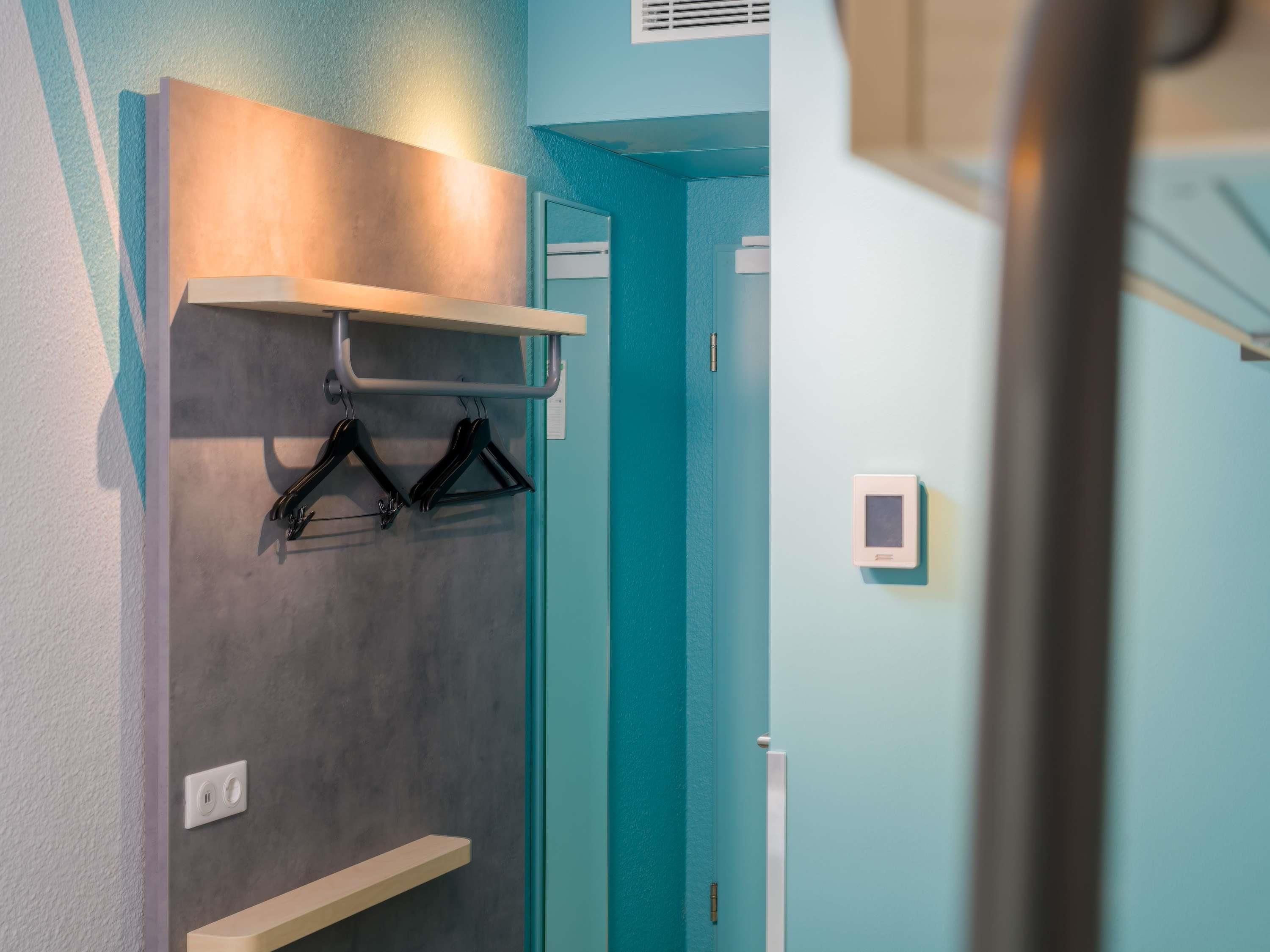 A hallway with a teal wall, a coat rack with hangers, a light switch, and a thermostat on the wall.