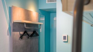 Ein Flur mit einer türkisfarbenen Wand, einem Kleiderständer mit Kleiderbügeln, einem Lichtschalter und einem Thermostat an der Wand.