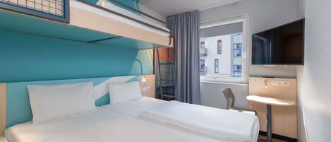 Habitación de hotel con literas, una televisión, una mesita y ventana con vistas a edificios.
