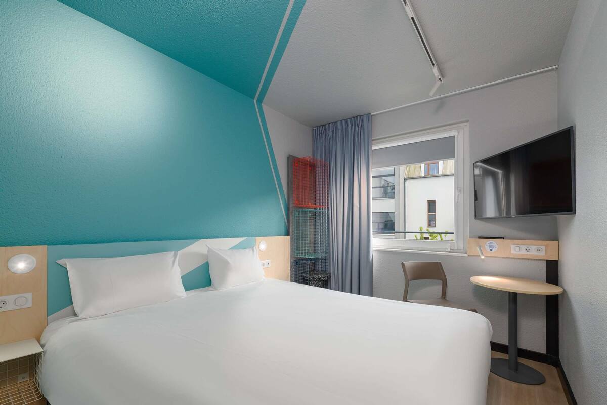 Una habitación de hotel moderna con una cama grande, un televisor, una mesita y una ventana con vistas al exterior.