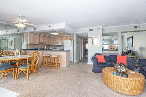 A spacious living area with a dining table, wicker ottoman, and a dark blue sofa.