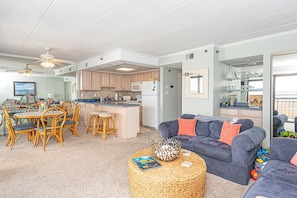 A spacious living area with a dining table, chairs, a sofa, and a kitchen in the background.