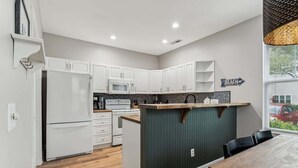 Una cocina moderna con armarios blancos, una isla central y vistas al exterior.
