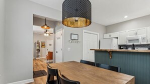 Una cocina moderna con armarios blancos, una mesa de comedor de madera y una lámpara colgante.