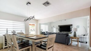 A modern living room with a dining area, a grey sofa, a TV, and a fireplace. - Delray Oasis: Pool, Gazebo & Beach Access (Delray Beach)