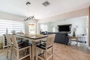 Una sala de estar moderna con comedor, un sofá gris, televisor y chimenea.