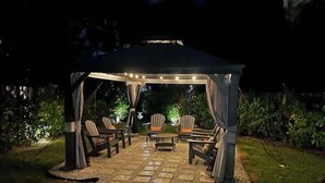 An outdoor patio with a covered seating area, a stone pathway, and ambient lighting. - Delray Oasis: Pool, Gazebo & Beach Access (Delray Beach)