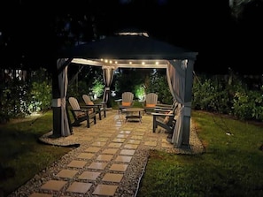 Un patio al aire libre con un área de estar cubierta, un sendero de piedra e iluminación ambiental.