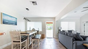 A modern living room with a grey sofa, a dining area with a table and chairs, and a kitchen visible through a doorway. - Delray Oasis: Pool, Gazebo & Beach Access (Delray Beach)