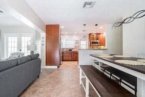 A modern kitchen with wooden cabinets, a dining table with placemats, and a grey sofa in a living area. - Delray Oasis: Pool, Gazebo & Beach Access (Delray Beach)