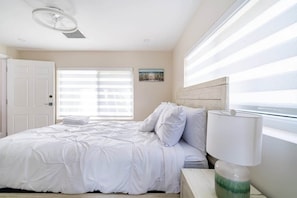 A bedroom with a bed, a nightstand, a lamp, a window with blinds, and a door. - Delray Oasis: Pool, Gazebo & Beach Access (Delray Beach)