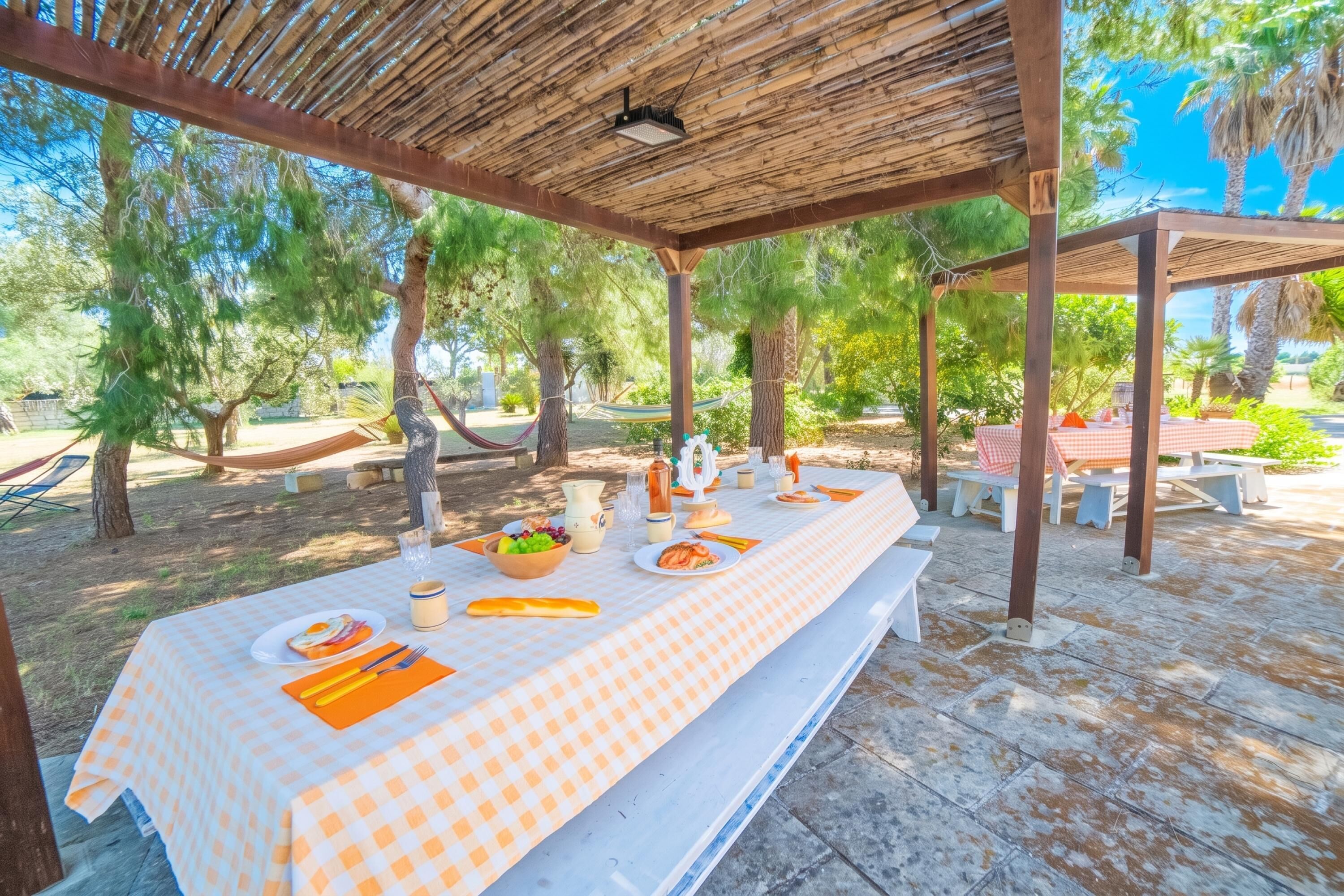 An outdoor dining area with a checkered tablecloth, wooden pergola, and picnic tables.