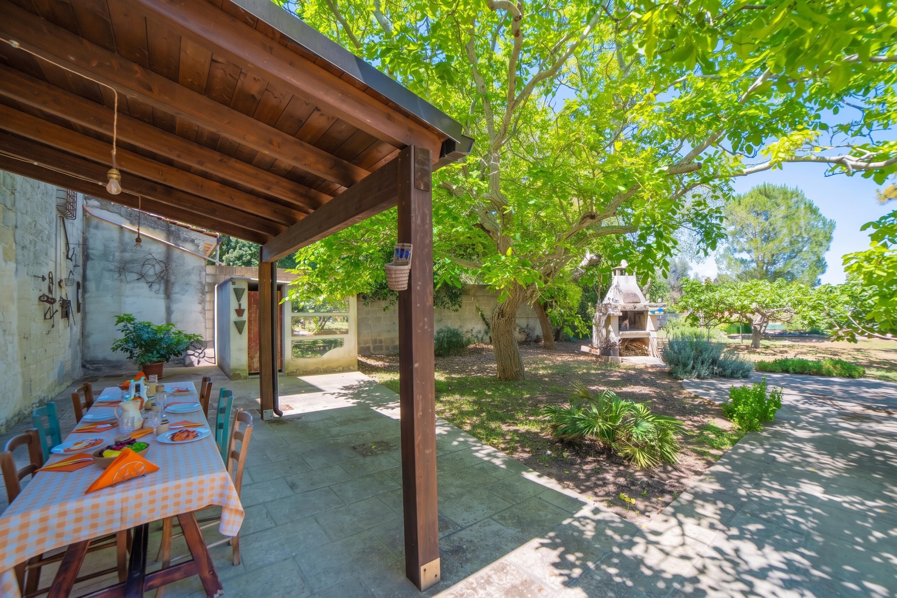An outdoor dining area with a checkered tablecloth, wooden chairs, and a pergola structure.