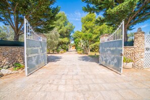A paved pathway leading to a gated entrance with a stone wall and trees on either side. - Masseria Le Palmentelle Pool And Garden (San Donato di Lecce)