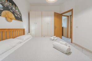 Un dormitorio con cama, cabecera de madera, un amplio armario y una puerta que da a otra habitación.
