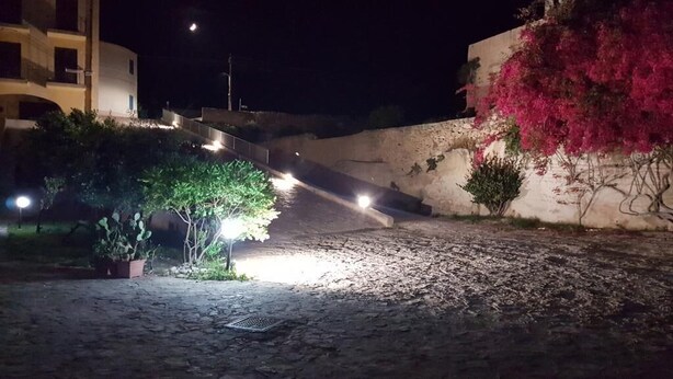 A cobblestone street at night with streetlights, a building with pink flowering vines, and a white building with balconies. - Apartament Zio Michele Centro dell'Isola (Favignana)