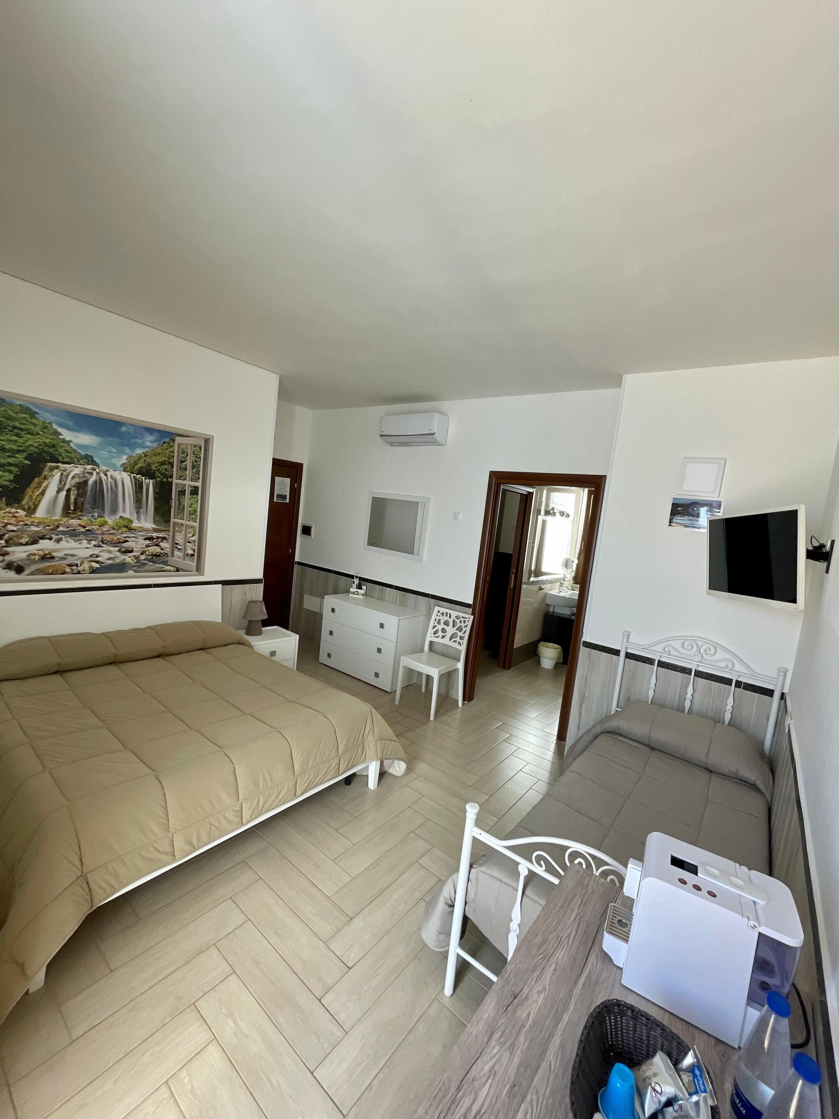 A hotel room with two beds, a desk, a chair, a TV, and a painting of a waterfall.