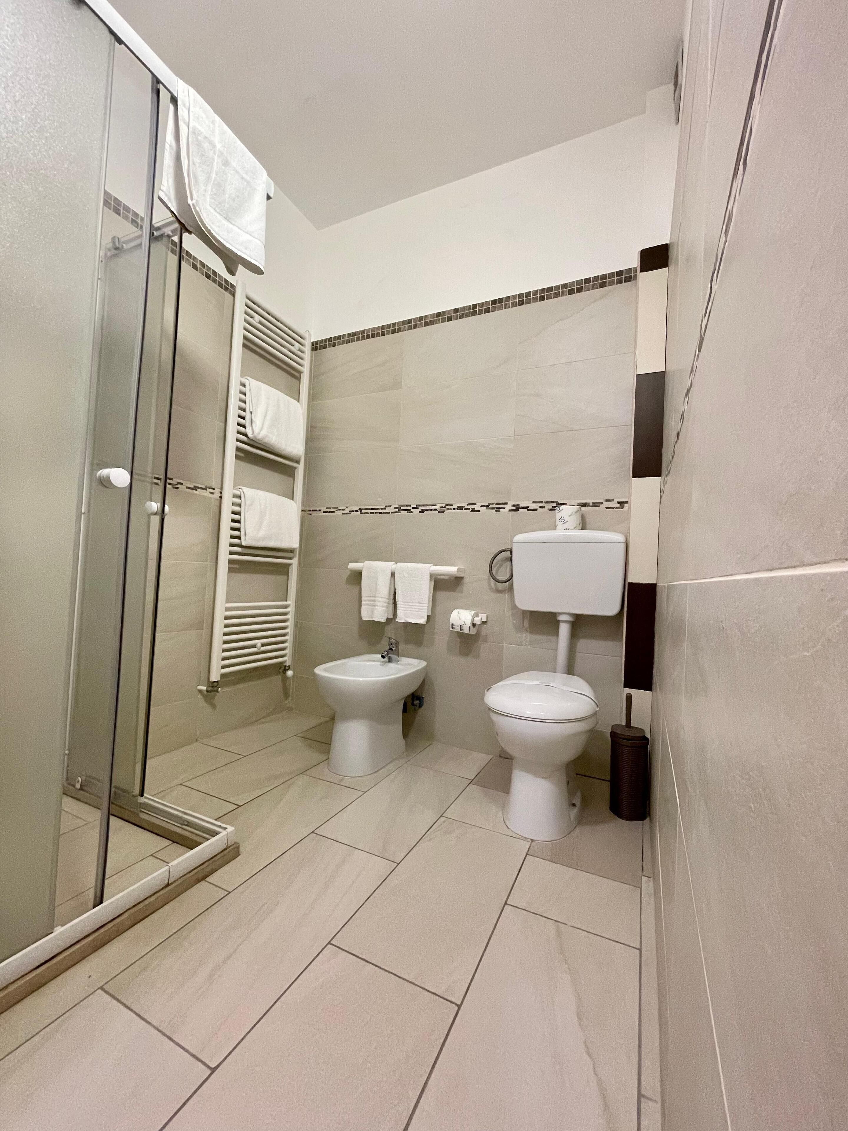 Ein modernes Badezimmer mit Duschkabine aus Glas, einem Bidet, einer Toilette und einem Handtuchhalter.