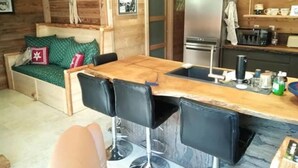Une pièce confortable, aménagée comme un chalet, avec une table à manger en bois, un canapé avec des coussins verts et un réfrigérateur.