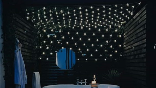 Un baño exterior privado con una bañera grande, rodeado por un sendero de grava y una guirnalda de luces.