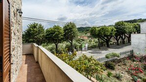 Een balkon met een stenen muur, betegelde vloer en uitzicht op een straat met bomen en een tuin met bloemen.