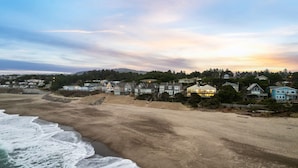 A coastal residential area with houses along the beach, a clear sky, and waves approaching the shore. - Azul Jewel Estate, Game Room, Movie Room & Beach (Depoe Bay)