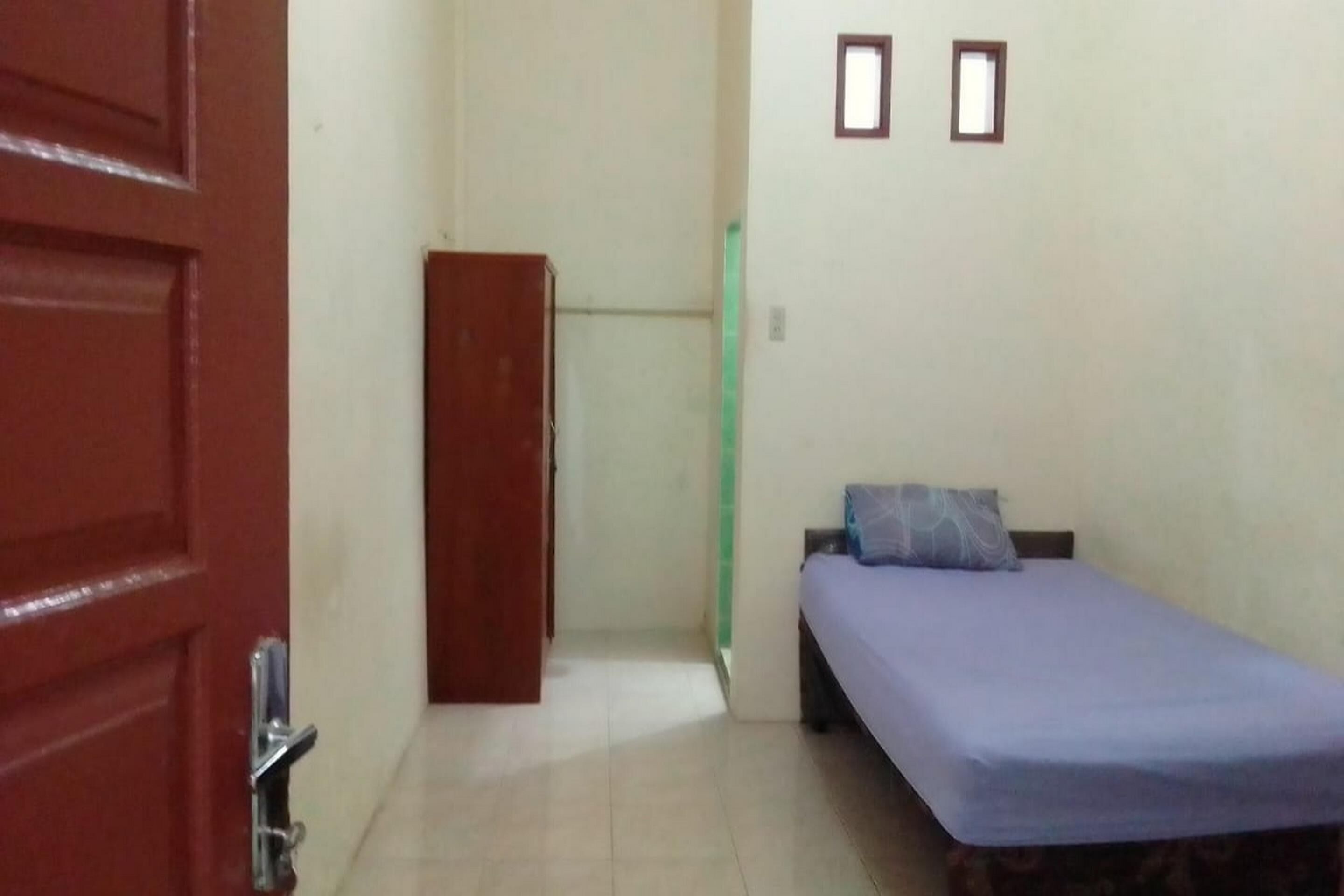 A small room with a bed, a door, and a wall-mounted shelf.