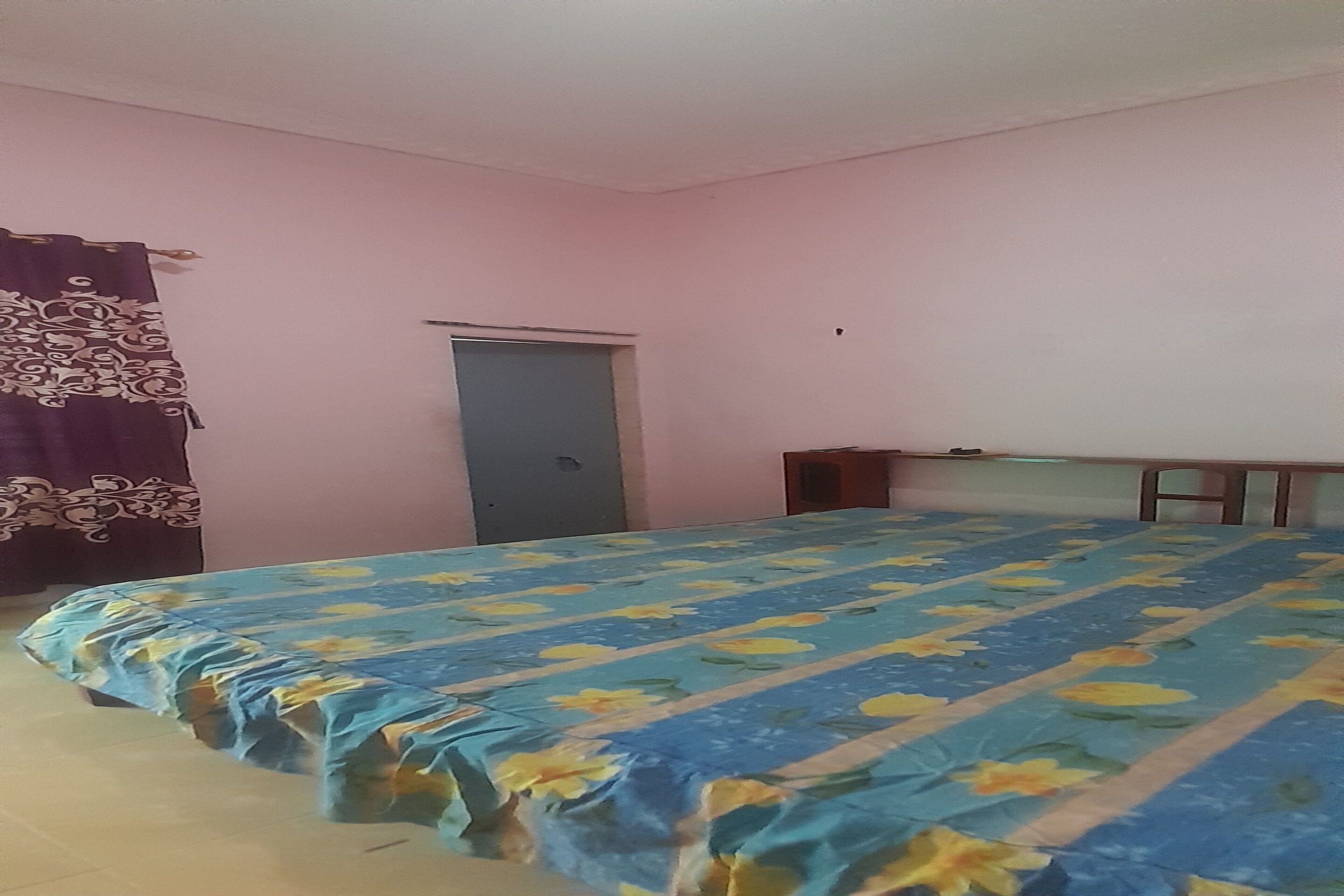 Una habitación con cama, puerta y una mesita.