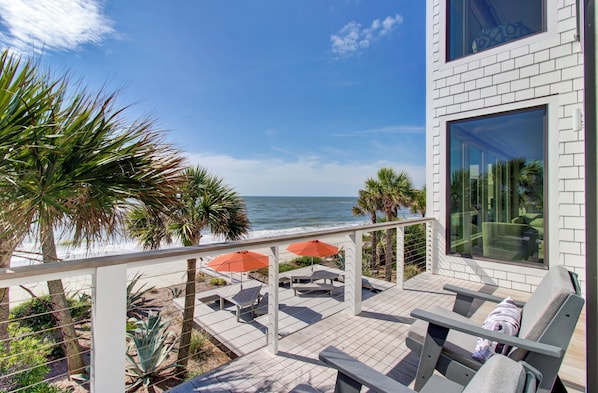 Un balcon aménagé avec du mobilier d’extérieur, une vue sur l’océan et un bâtiment moderne doté de grandes fenêtres.