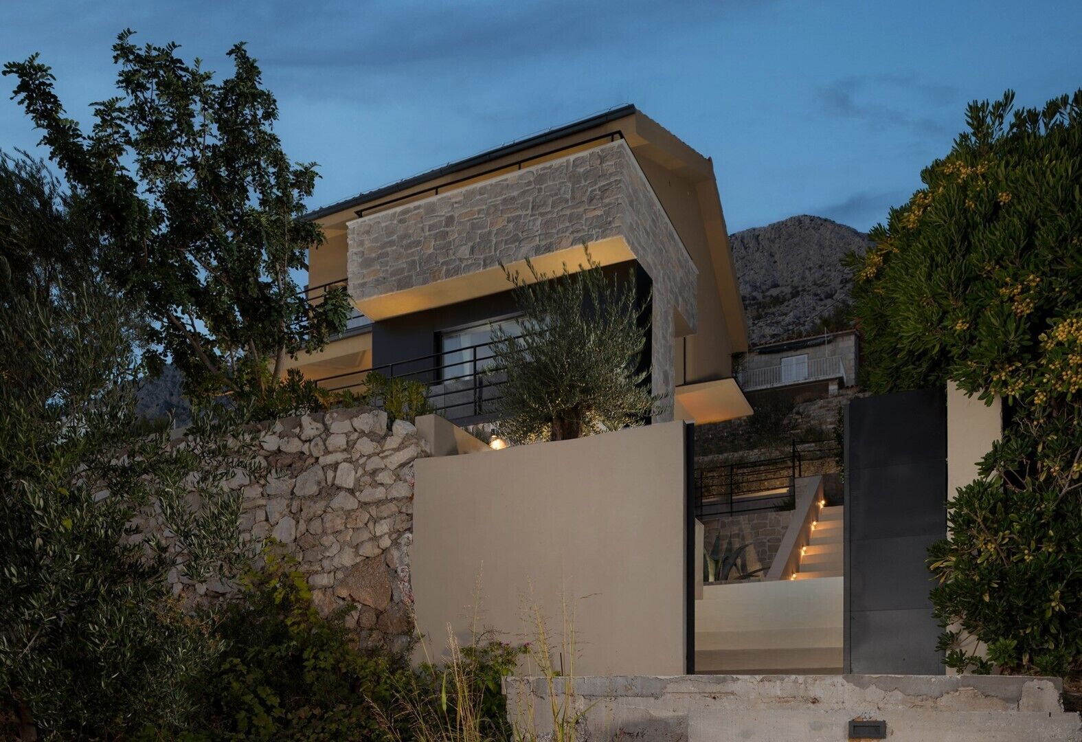 Une maison moderne avec une façade en pierre, une grande fenêtre et un escalier menant à un étage supérieur.
