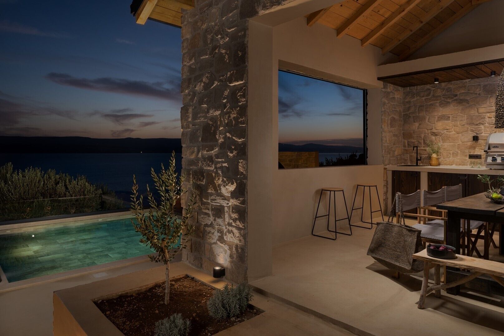 An outdoor patio with a stone wall, a pool, and a dining area with chairs and a table.