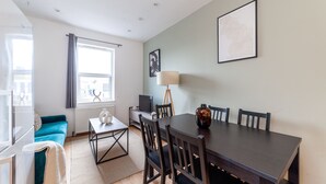 A modern living room with a dining table, chairs, a sofa, a TV, and a lamp.