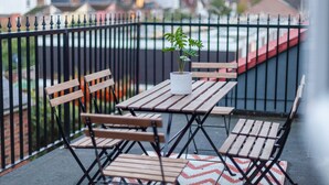 A balcony with a table and chairs, a potted plant, and a view of buildings in the background.
