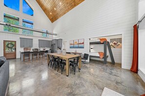 A spacious kitchen with a dining area, large windows, and a high ceiling.