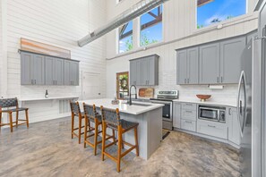 A spacious kitchen with grey cabinets, a central island with bar stools, and a large window.