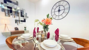 Un espace repas moderne avec une table en verre, des chaises orange et une grande horloge murale.