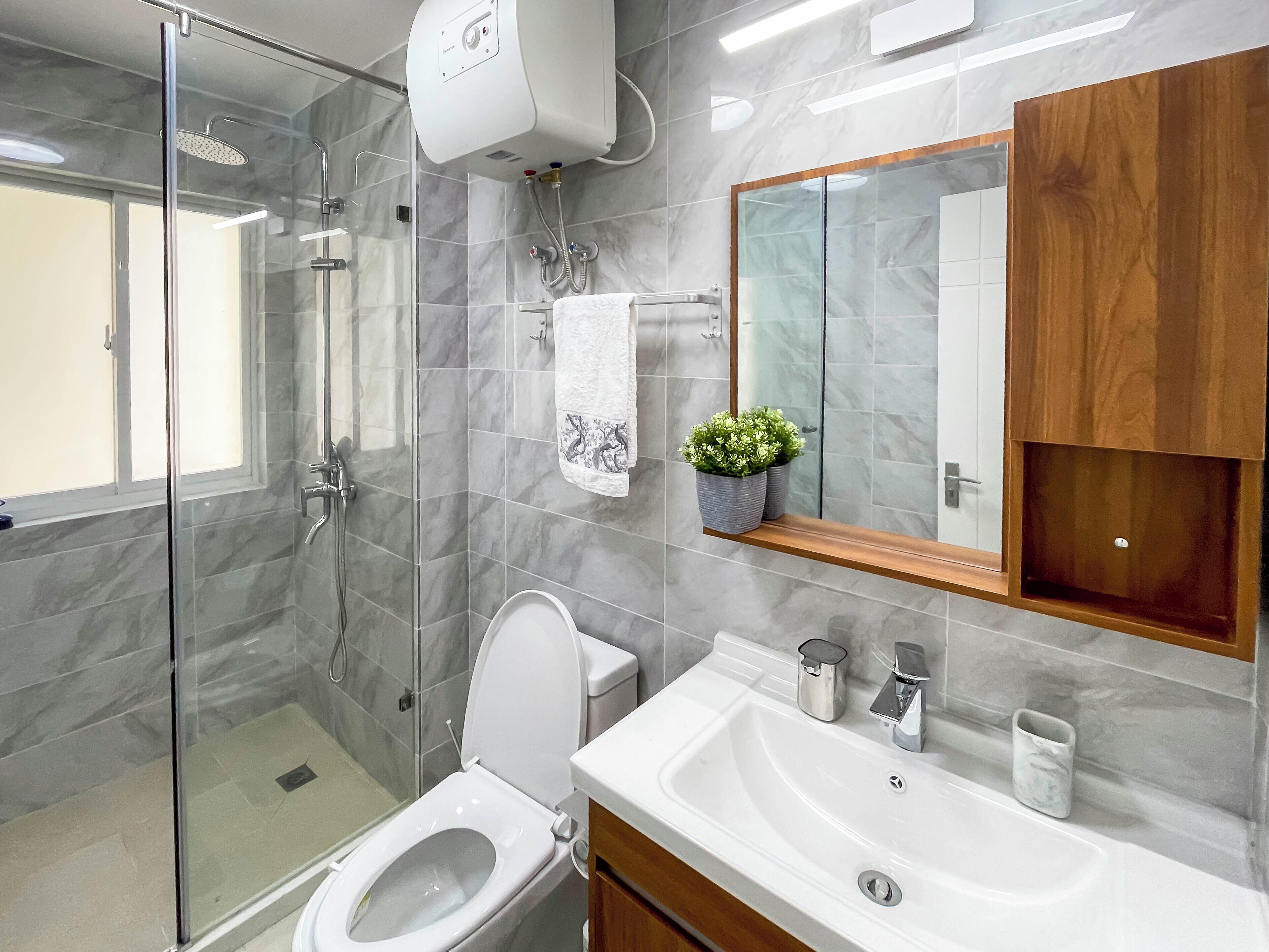 A modern bathroom with a glass shower enclosure, a toilet, a sink with a mirror, and a wooden cabinet.