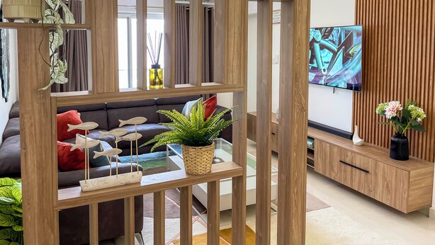 Un salon moderne avec un canapé d’angle, un téléviseur, des éléments de décoration en bois et une plante en pot.