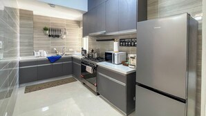 Une cuisine moderne dotée d’appareils électroménagers en acier inoxydable, de meubles de rangement gris et d’un dosseret carrelé.