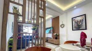 Un salon moderne avec un téléviseur, une cloison en bois et un coin repas avec de l’assiette et des couverts.