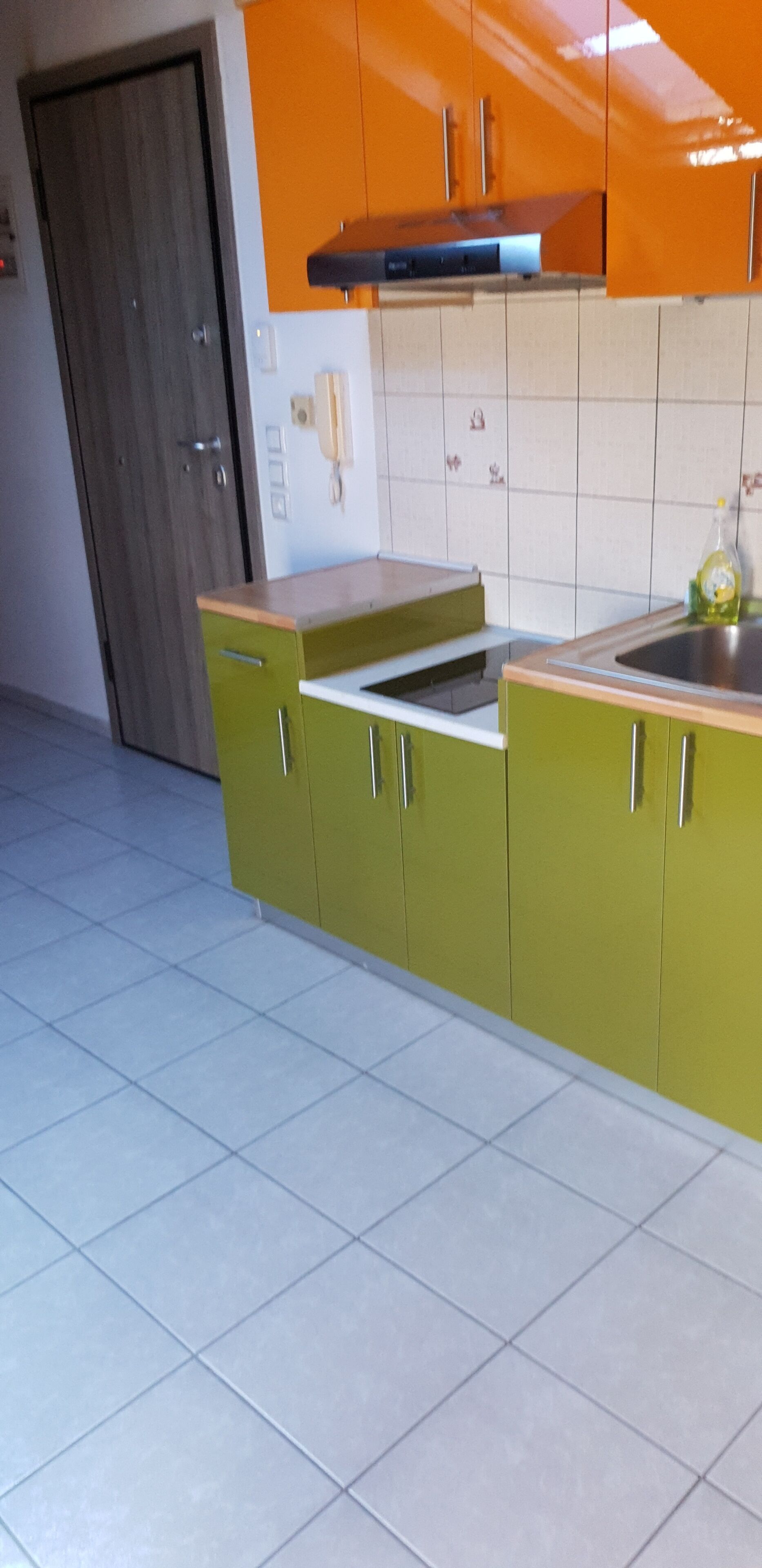 A kitchen with green cabinets, a wooden door, and a tiled backsplash.