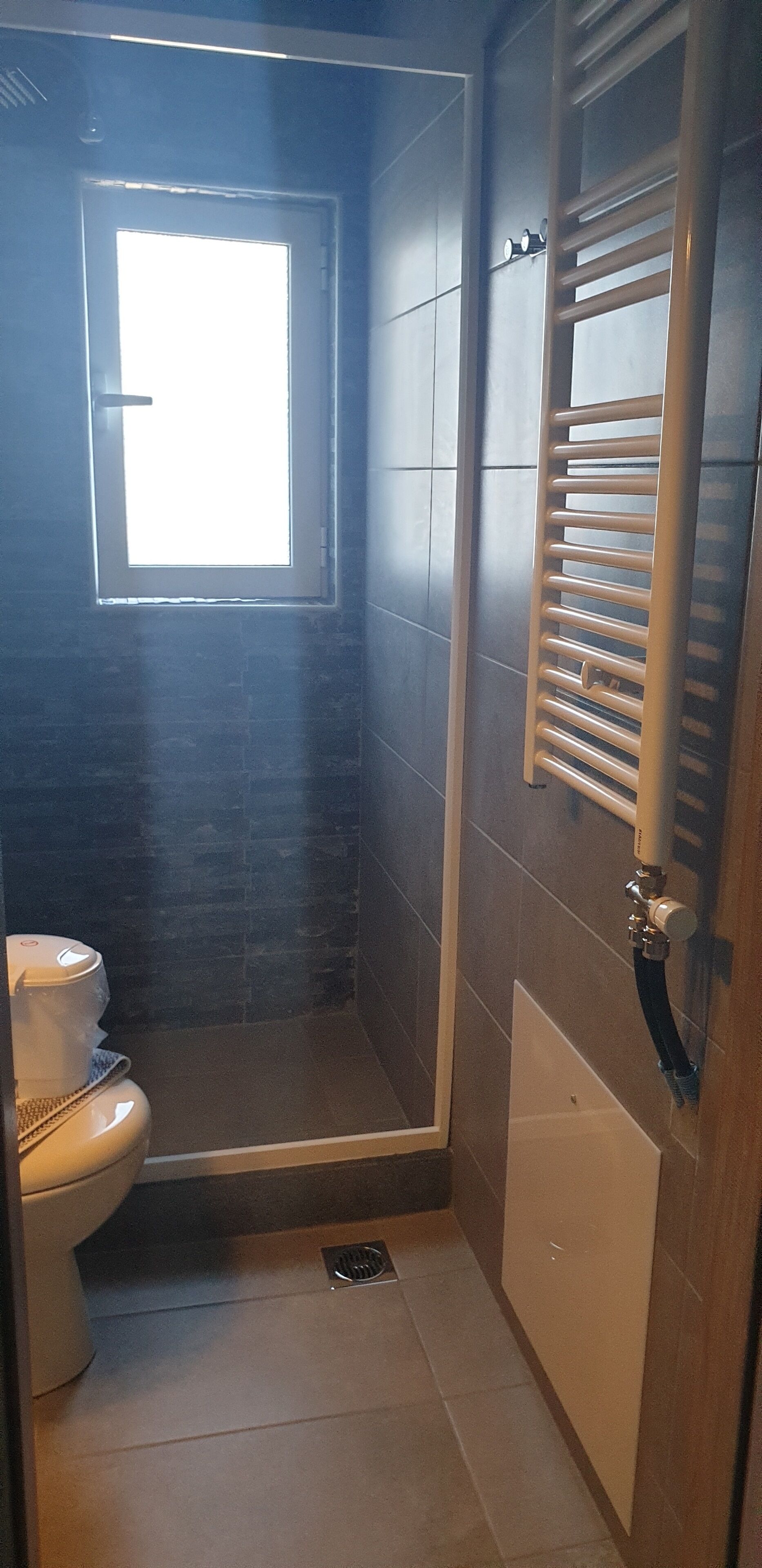 A small bathroom with a toilet, a shower with a glass door, and a window providing natural light.