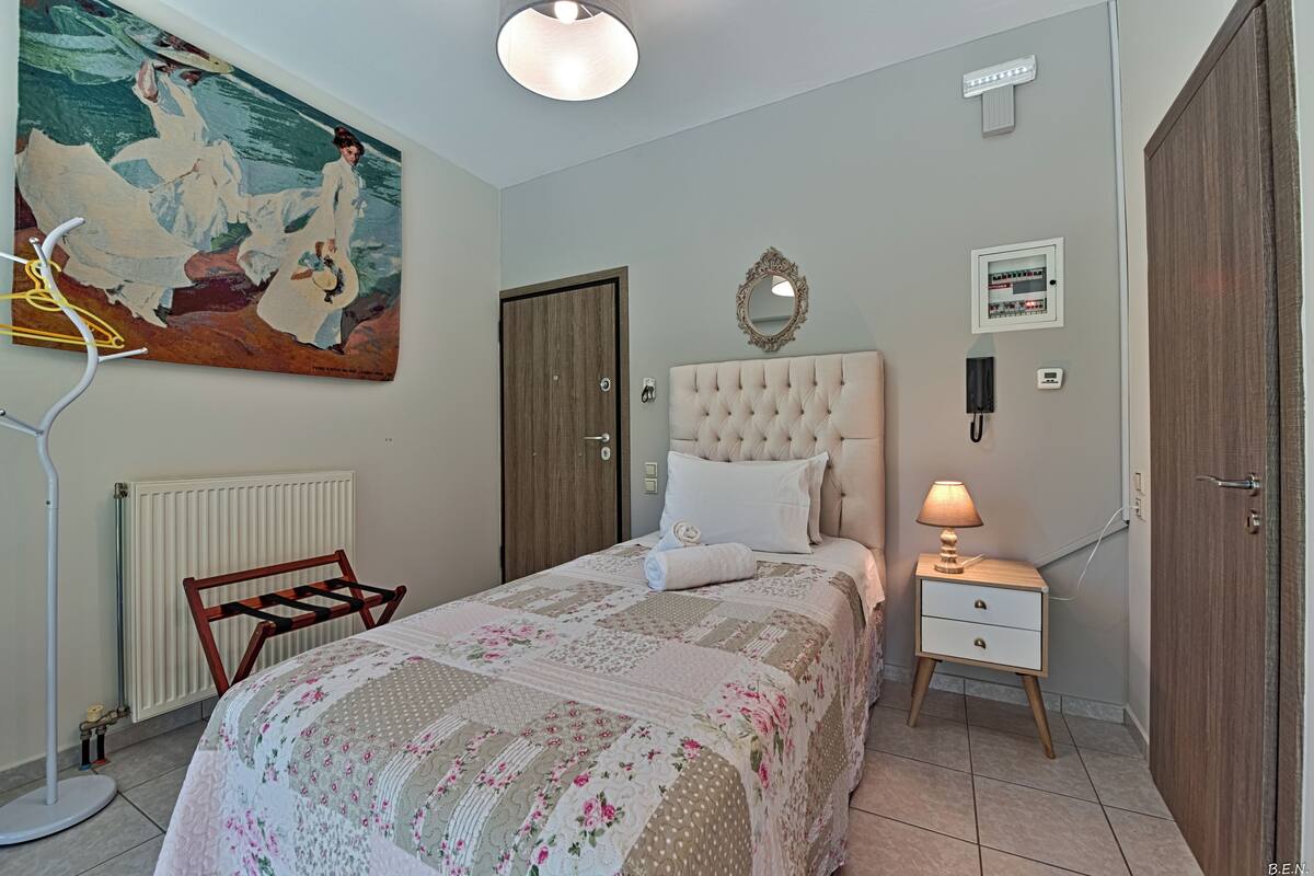A bedroom with a bed, a nightstand, a radiator, a painting, a mirror, and a door.