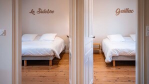 Habitación de hotel con dos camas, suelo de madera y un espejo que refleja el ambiente.