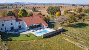 Una casa grande con piscina, un patio con mobiliario exterior y vistas al campo circundante.