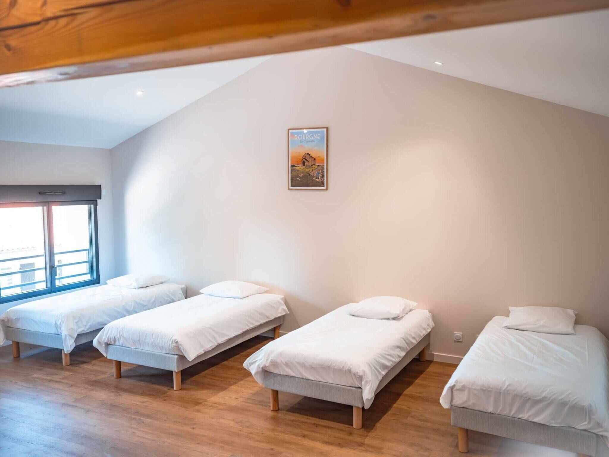 A room with three single beds, a large window, and a painting on the wall.