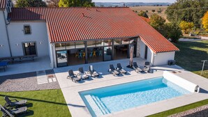 Una casa moderna con piscina, mobiliario exterior y techo de tejas rojas.