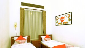 Une chambre d’hôtel avec deux lits, une fenêtre avec des rideaux, une table de chevet et un cadre photo fixé au mur.